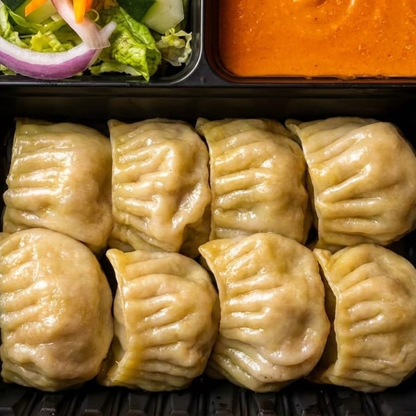 Eight steamed dumplings with a side of salad and orange sauce in a black takeout container.