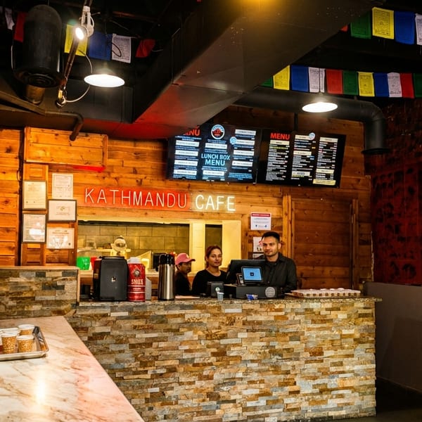 Two staff members stand behind the counter at Kathmandu Cafe, with menus displayed above.