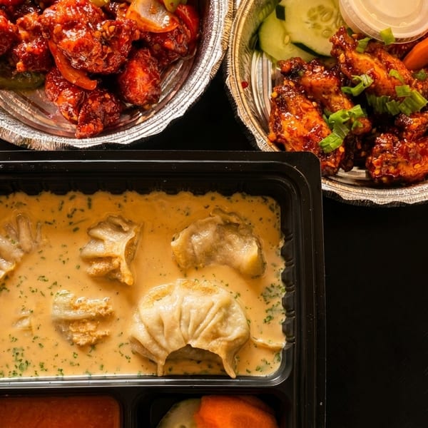 Top-down view of three takeout containers with chili chicken, chicken wings, and momos in sauce.