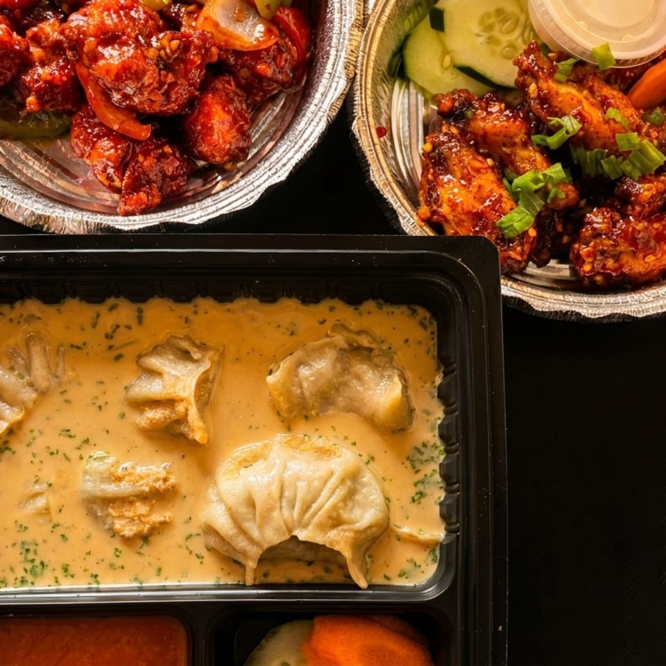 Top-down view of three takeout containers with chili chicken, chicken wings, and momos in sauce.