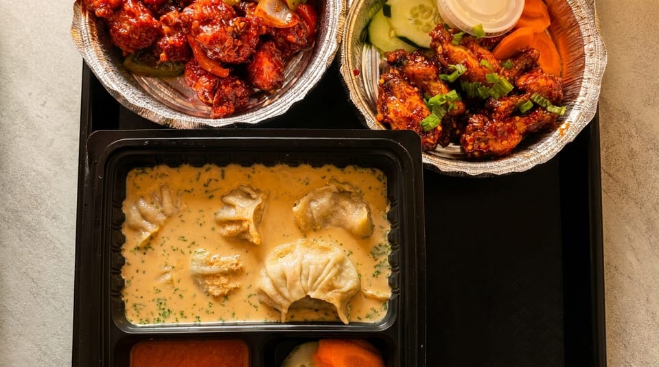 Top-down view of three takeout containers with chili chicken, chicken wings, and momos in sauce.