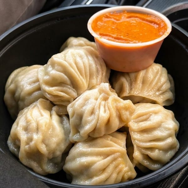 Steamed momos in a black bowl with a side of orange dipping sauce, in a car's cup holder.