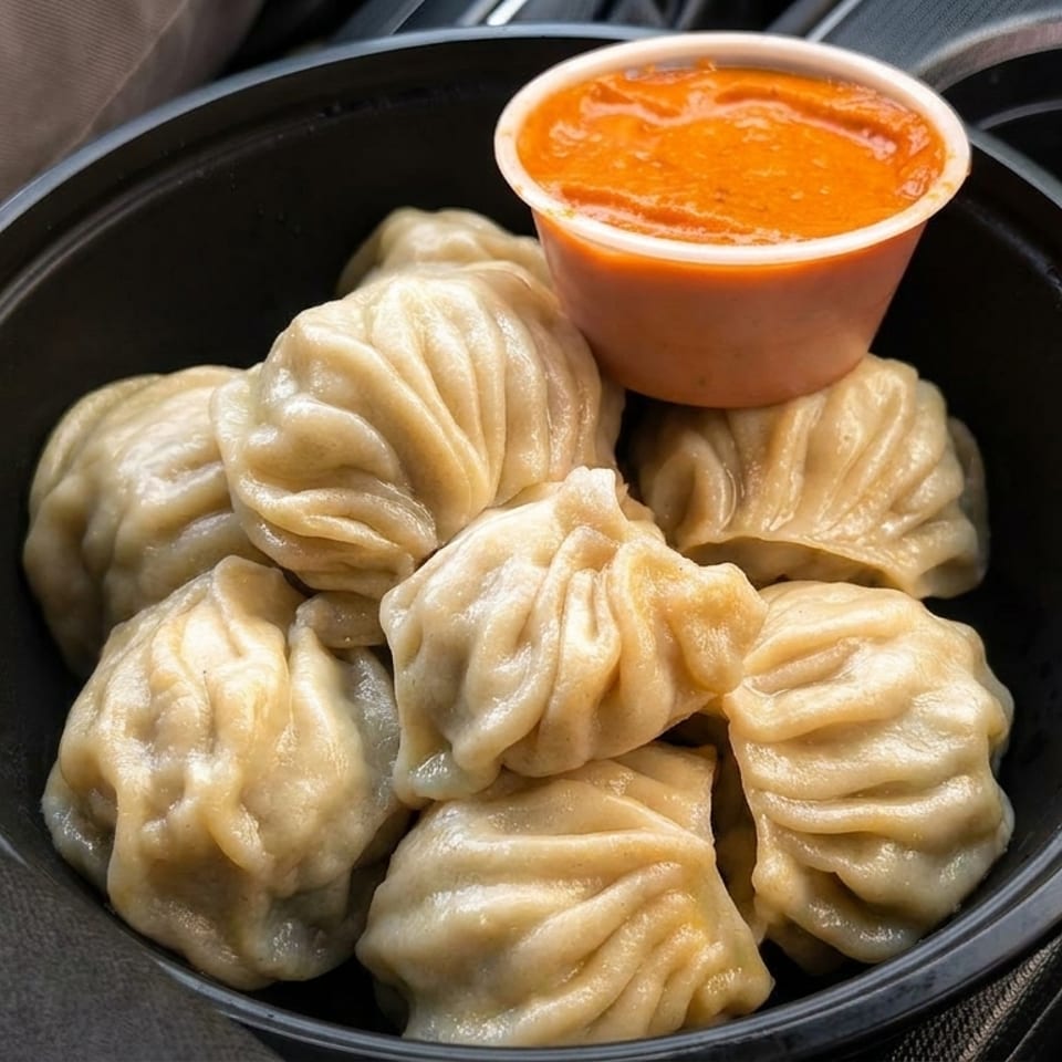 Steamed momos in a black bowl with a side of orange dipping sauce, in a car's cup holder.
